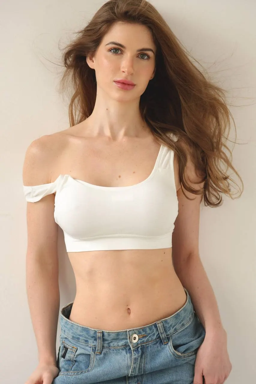 intensity Woman posing in a white sports bra and denim jeans.