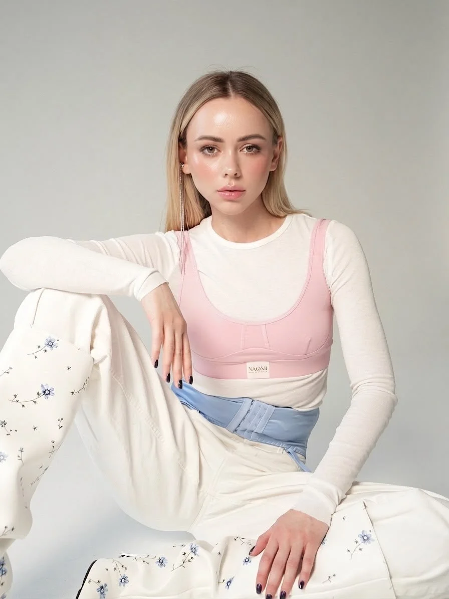 Woman sitting in white top, pink bralette and floral trousers.