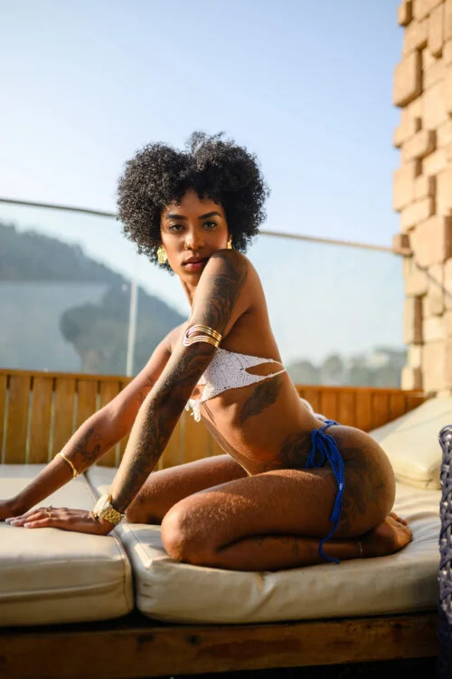 Tattooed woman with an afro in a white crochet bikini