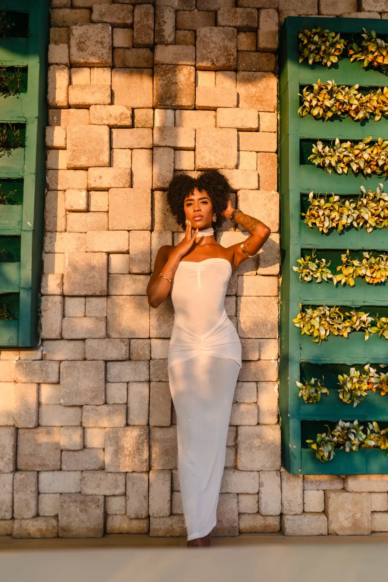 Woman in white dress posing against a textured stone wall