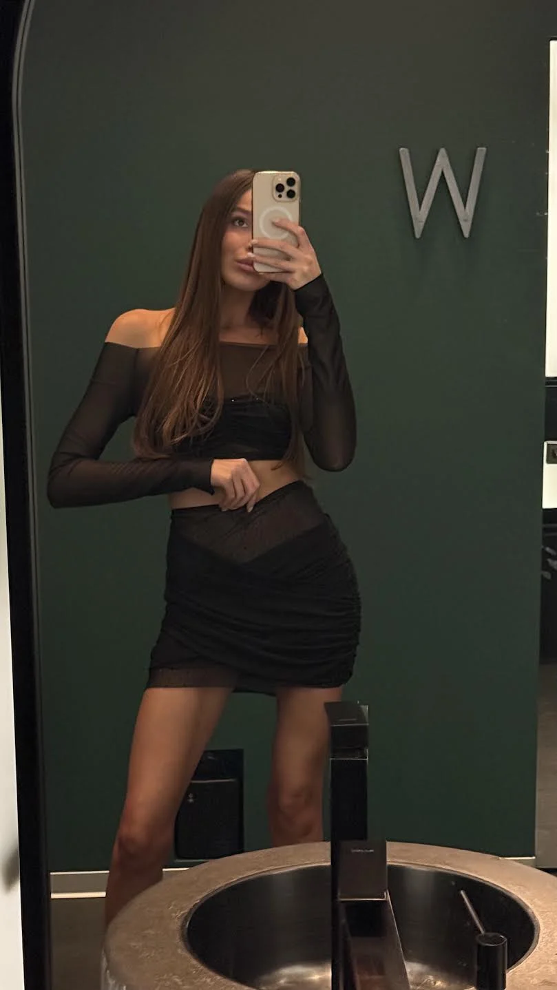 Woman in black two-piece outfit taking a mirror selfie.