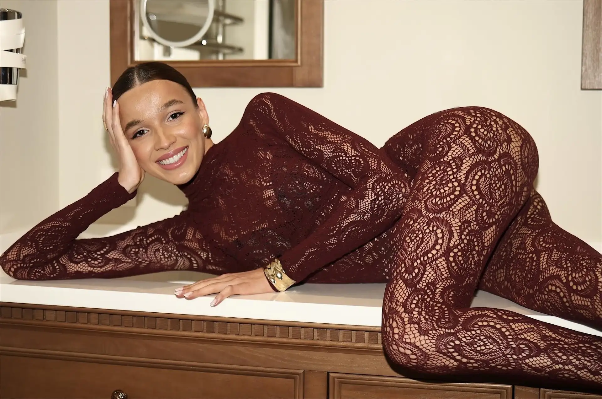Woman in burgundy lace bodysuit reclining and smiling