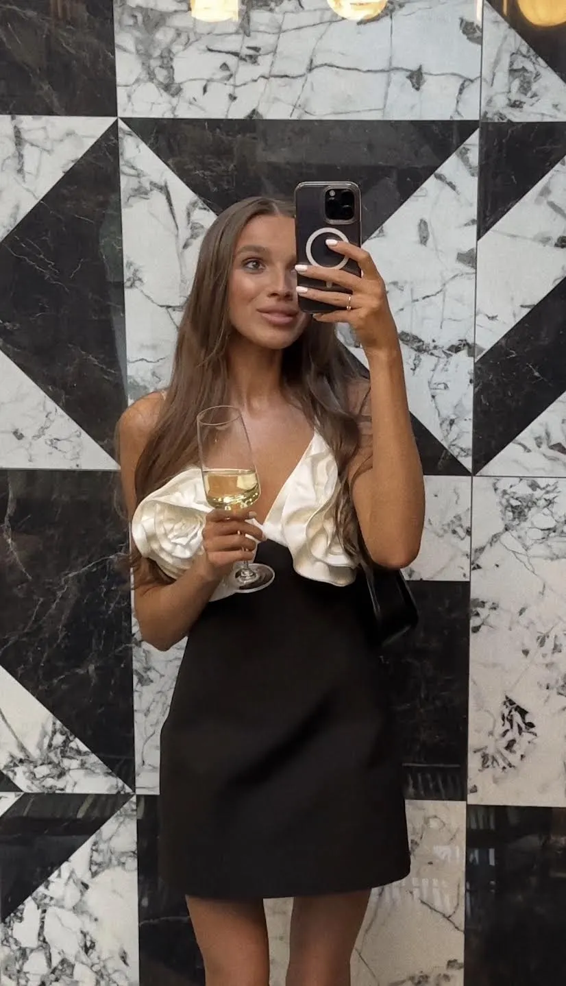 Woman in monochrome ruffle dress taking a mirror selfie.