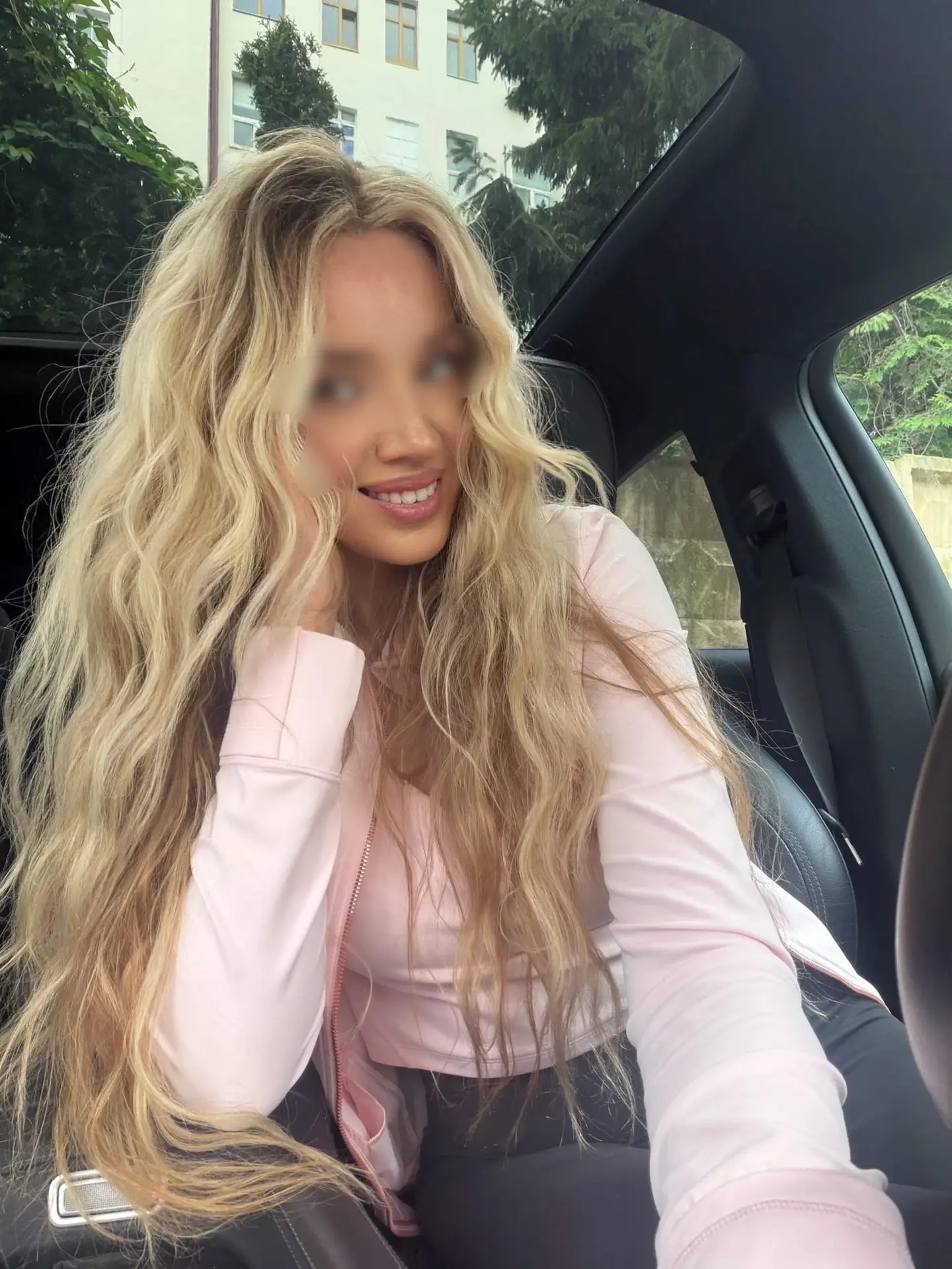 Smiling woman with long wavy blonde hair inside a car.