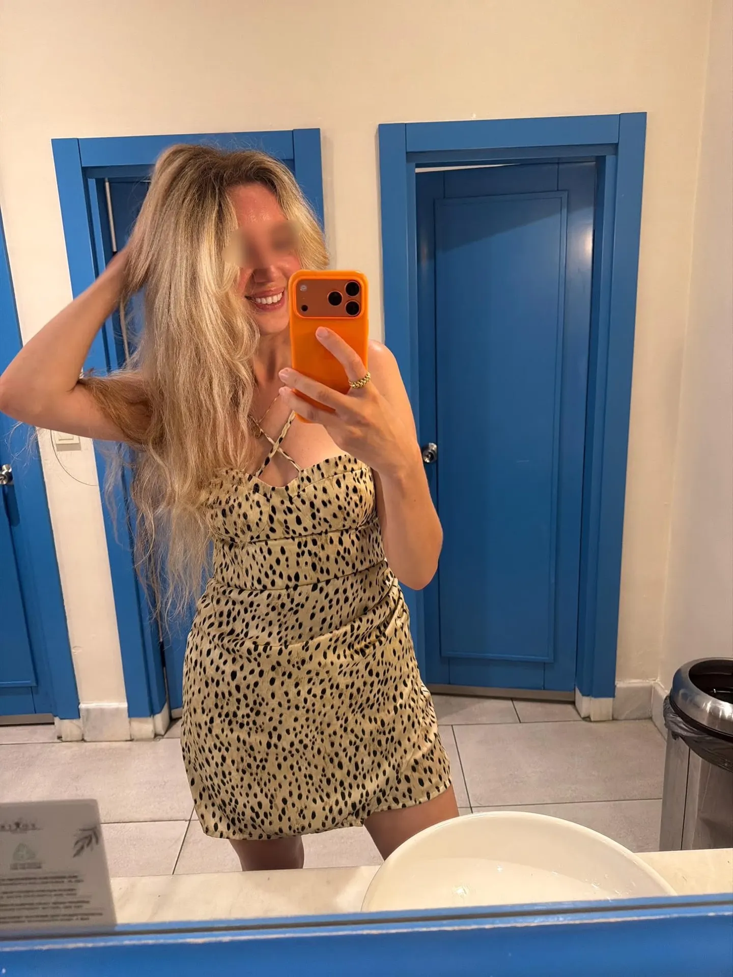 Woman in leopard-print dress taking selfie by blue doors.