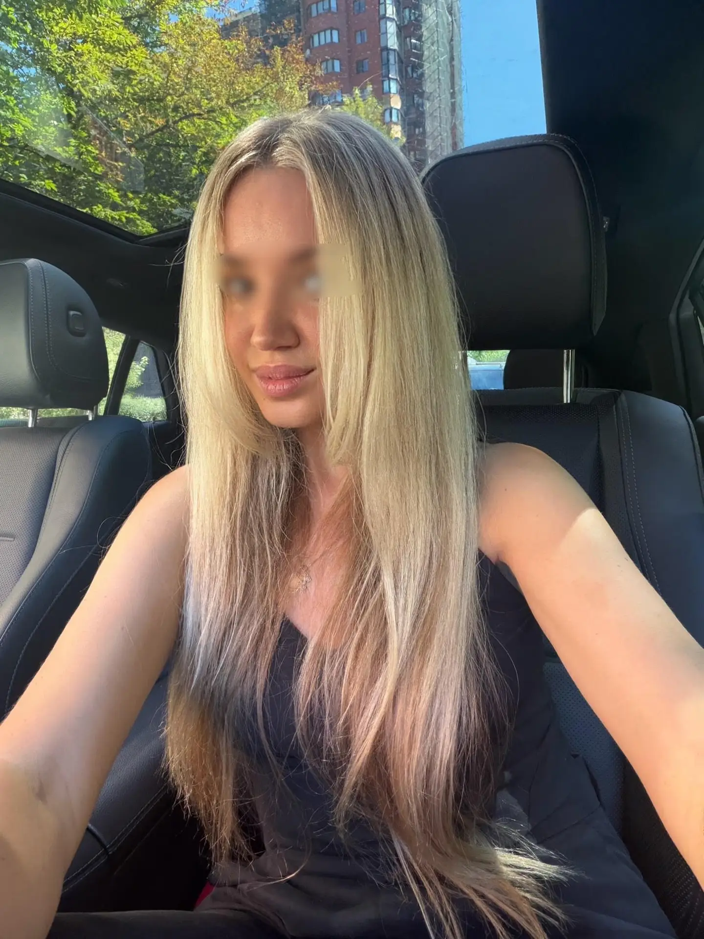 Young woman with long blonde hair sitting in a car.