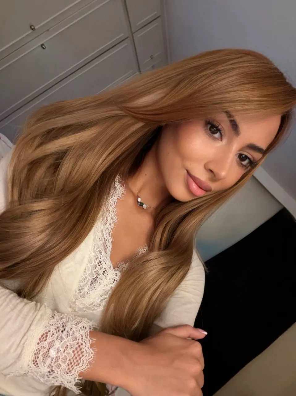Woman with long caramel-coloured hair wearing a lace top.