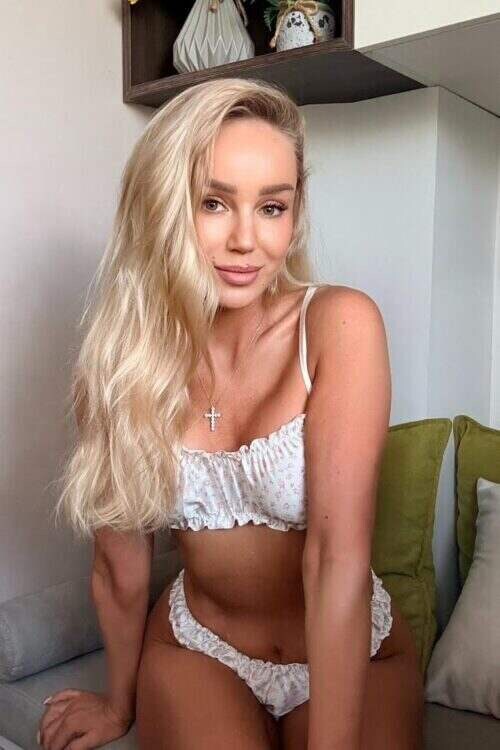Blonde woman in white floral lingerie sitting on a sofa.