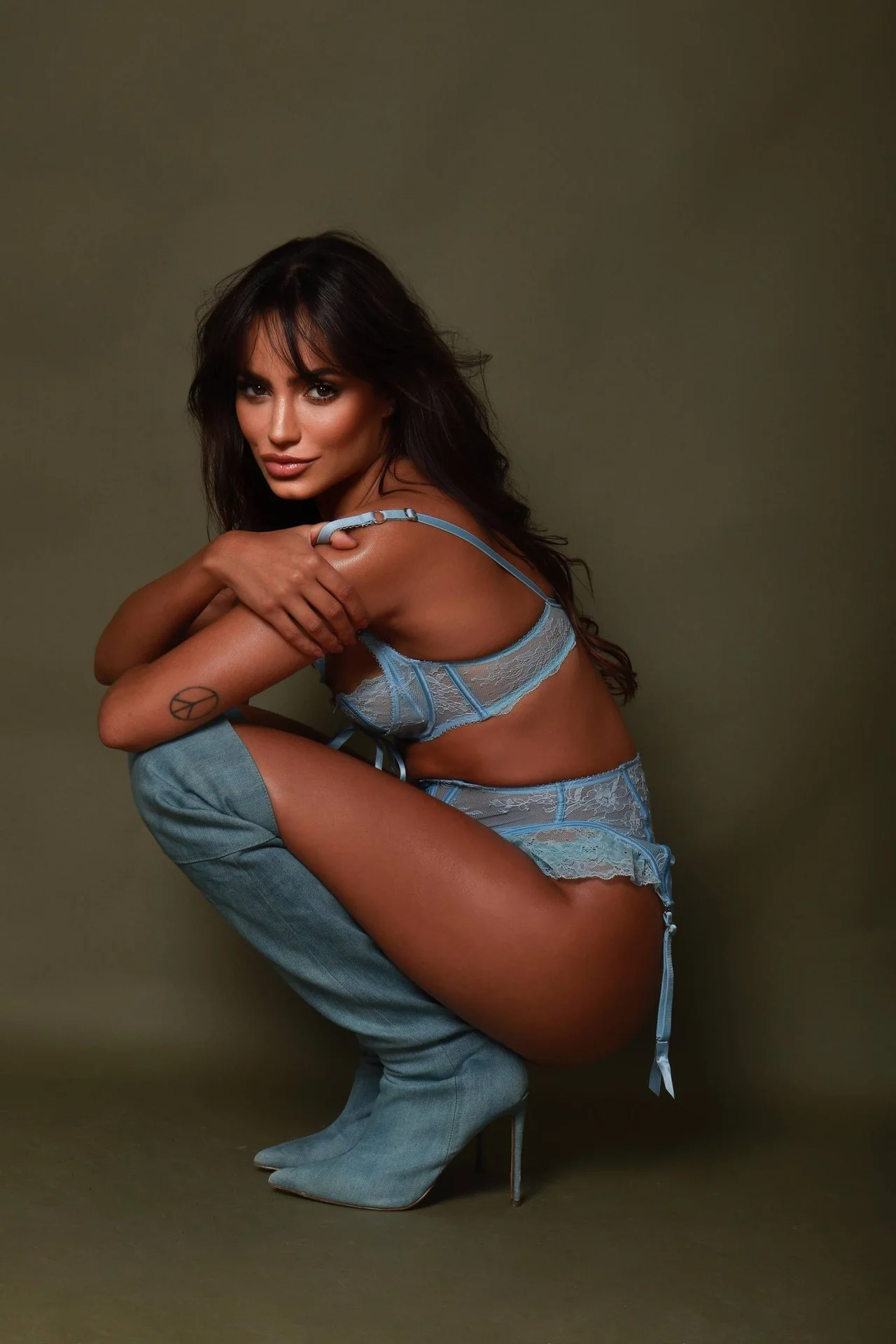 Woman in blue lace lingerie and denim boots crouching.