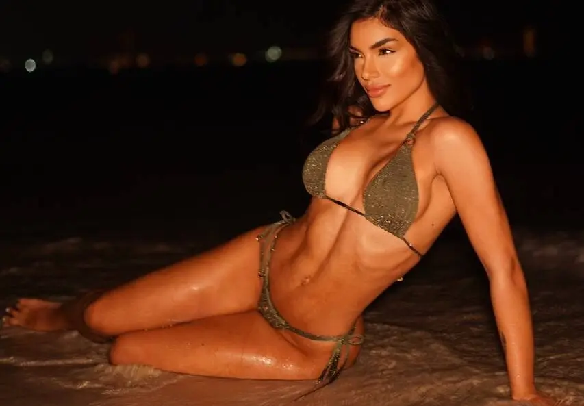 Woman in dark green bikini reclining on a night beach.