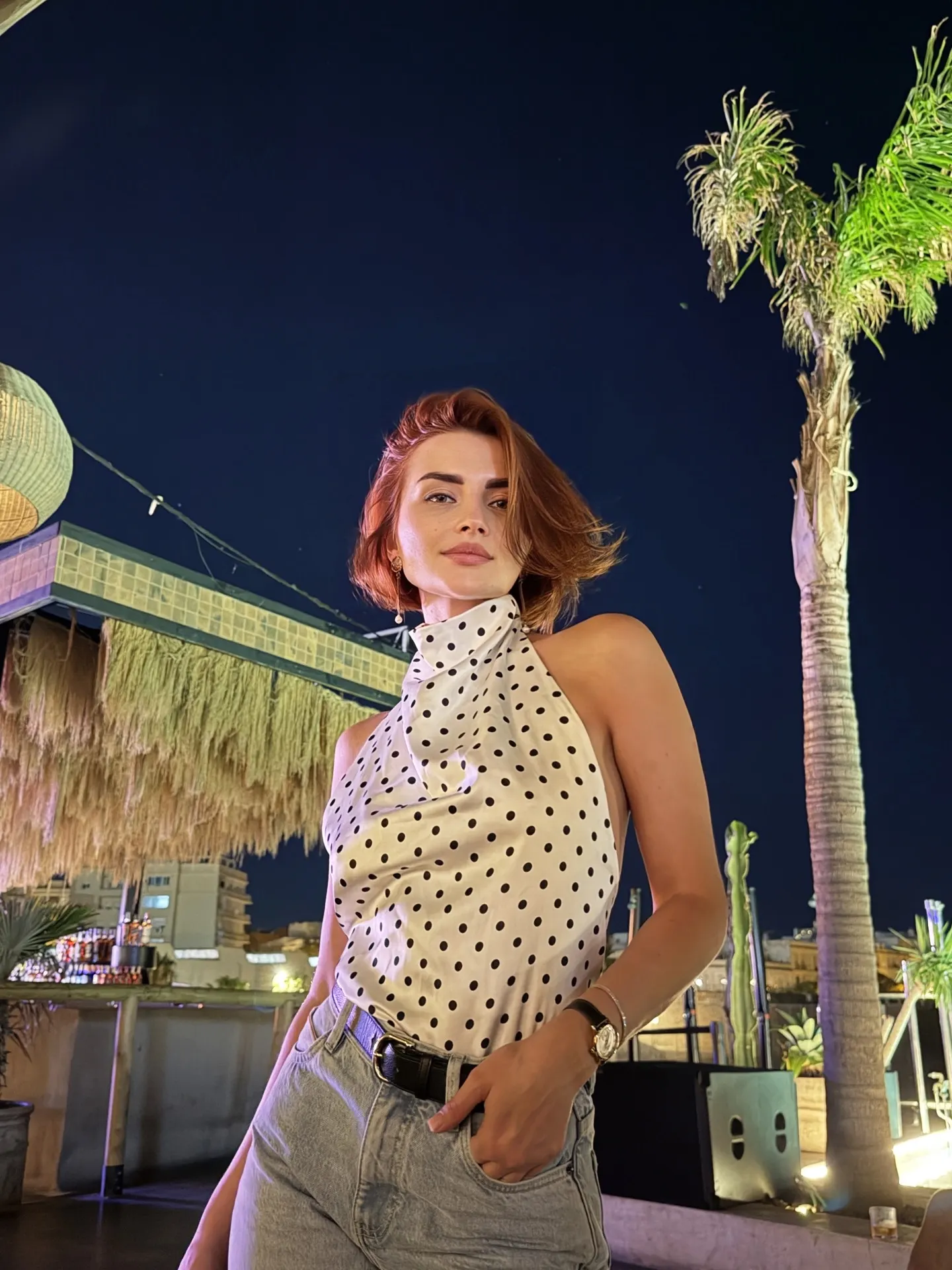 Redheaded woman in polka dot top at night rooftop bar.