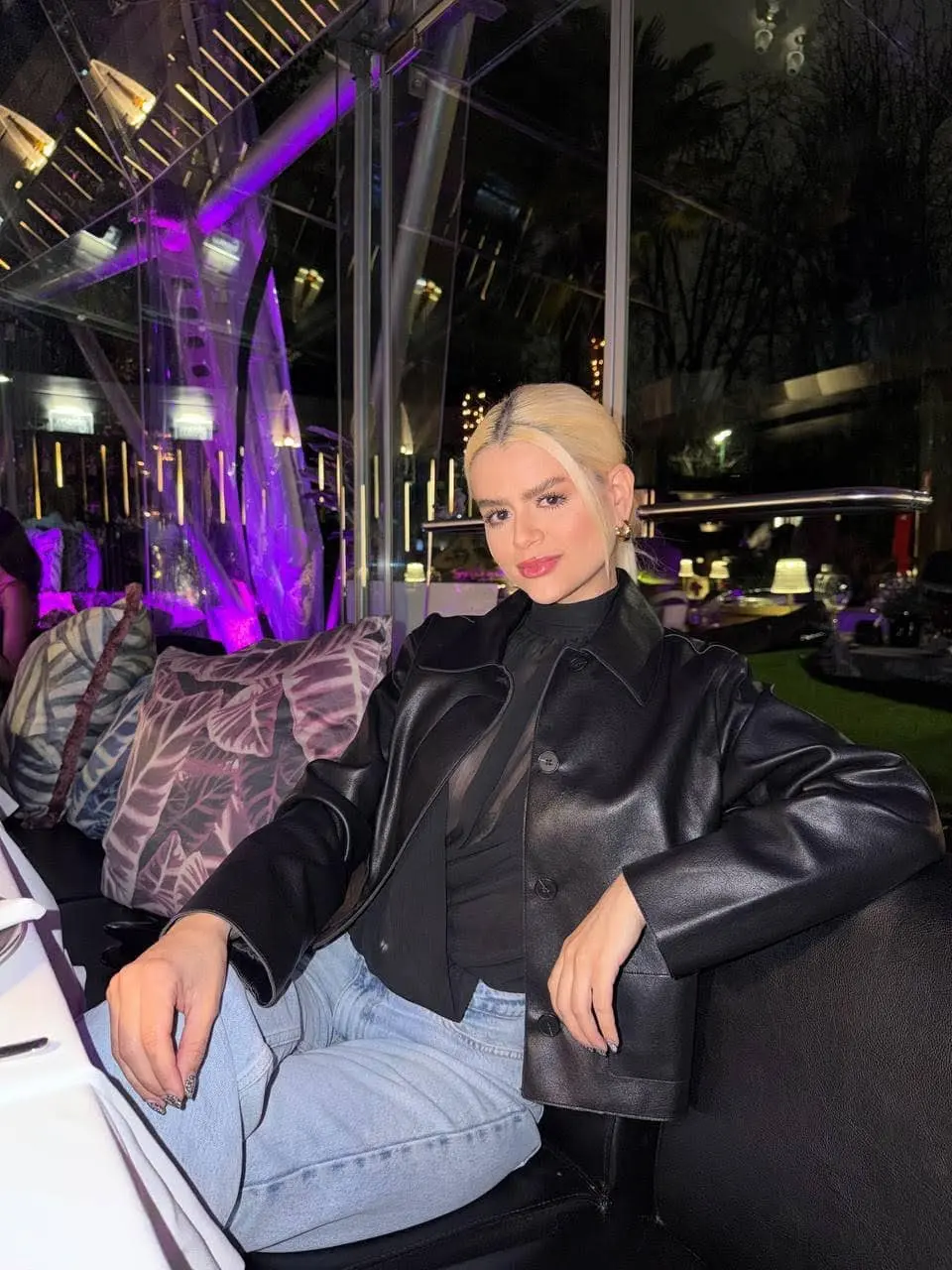 Blonde woman in a black leather jacket at a restaurant.
