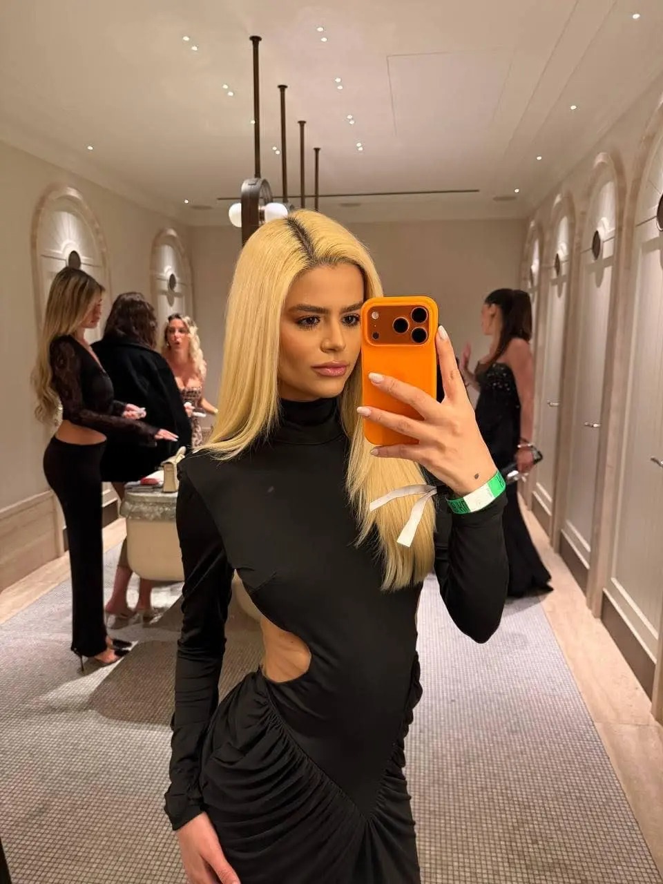Blonde woman in black cutout dress taking mirror selfie.