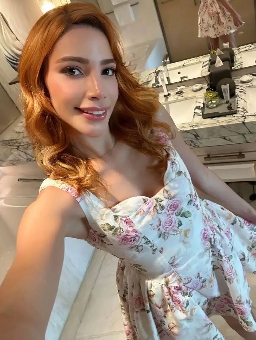 Woman in floral dress taking selfie in marble bathroom.