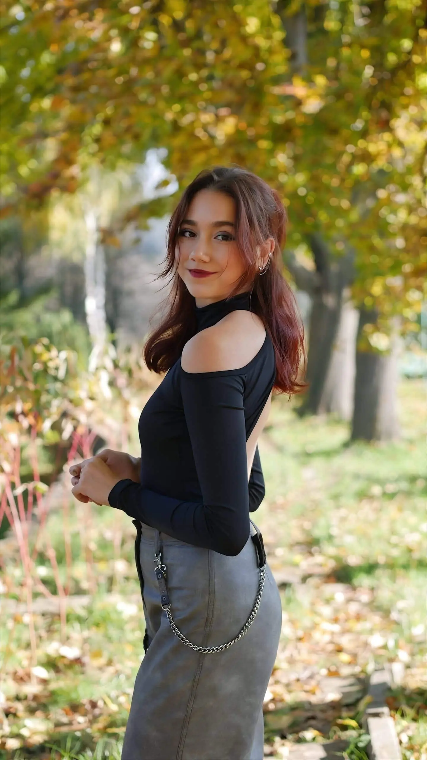 A woman in a black top posing in an autumn park.