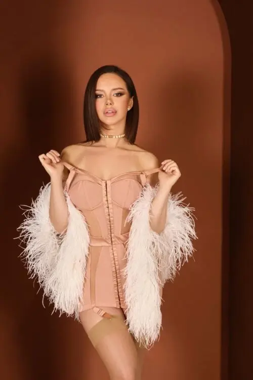 Woman in peach corset dress and white feather shawl.
