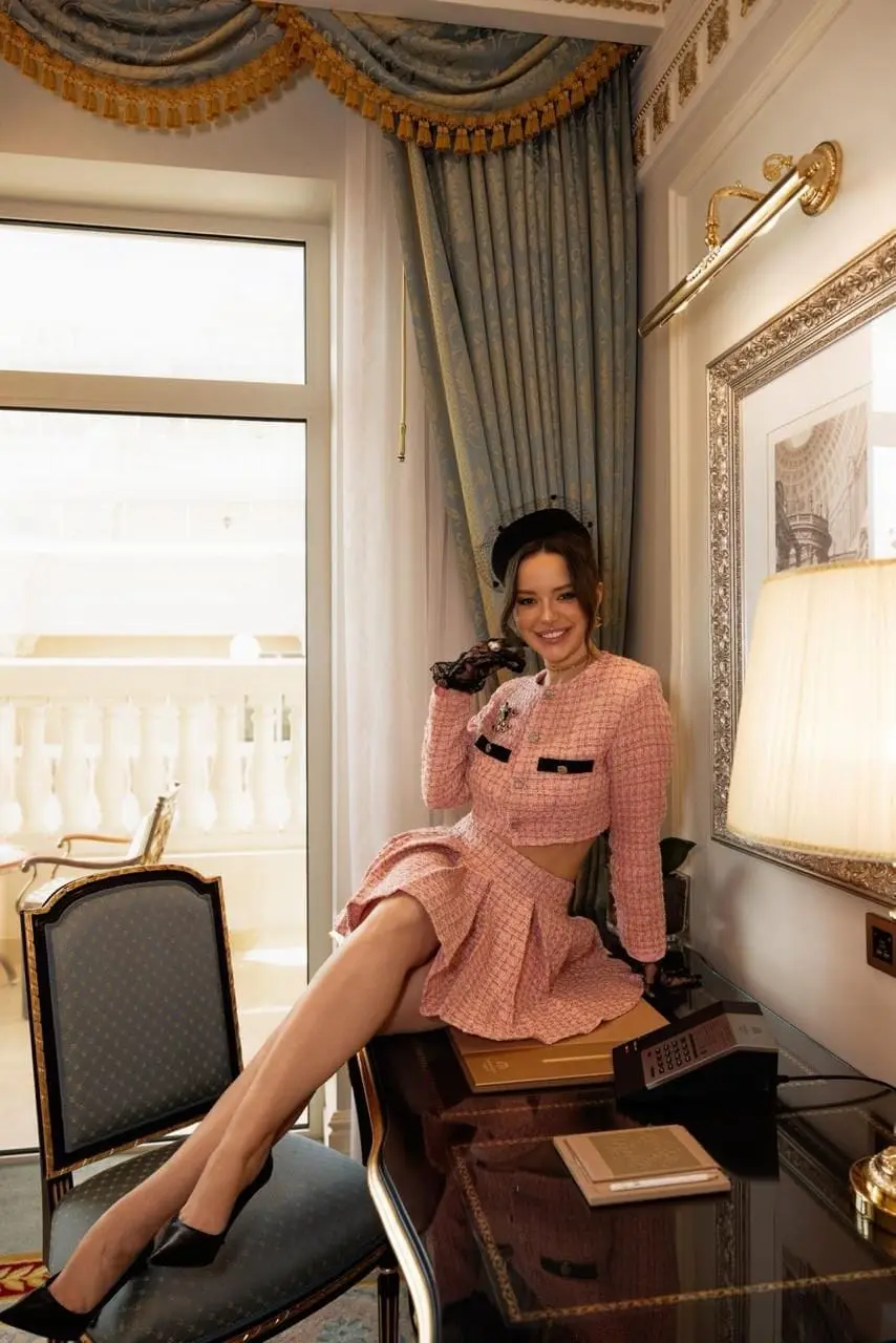 Elegant woman in pink tweed two-piece posing indoors.