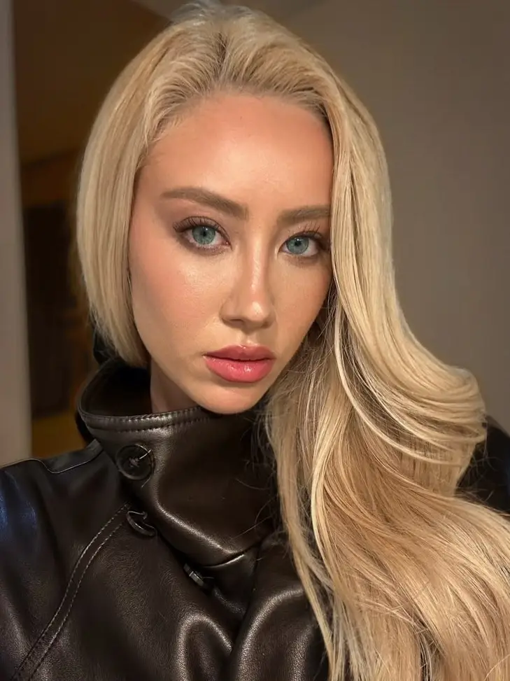 Blonde woman with blue eyes wearing a leather jacket.