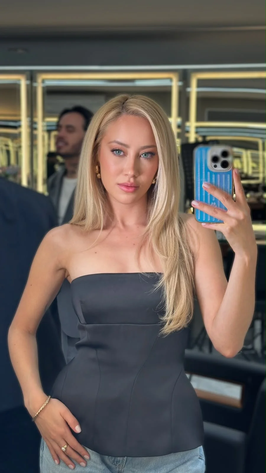 Blonde woman in black strapless top taking a mirror selfie.