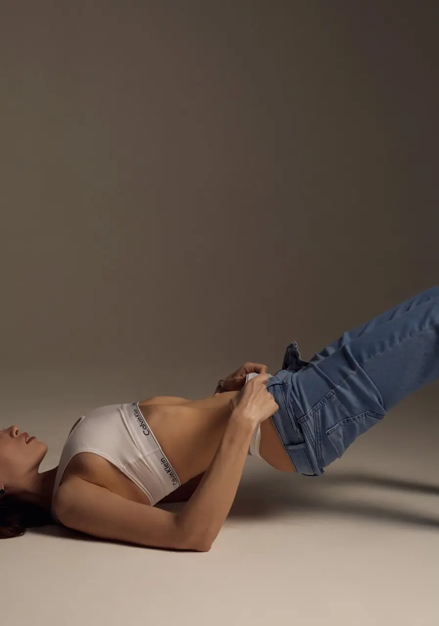 Woman posing in a white sports bra and blue jeans.