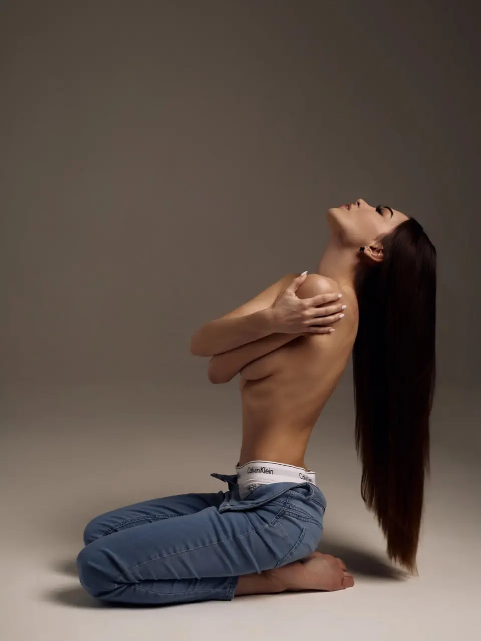 Woman kneeling in jeans with long hair, tilting head back.