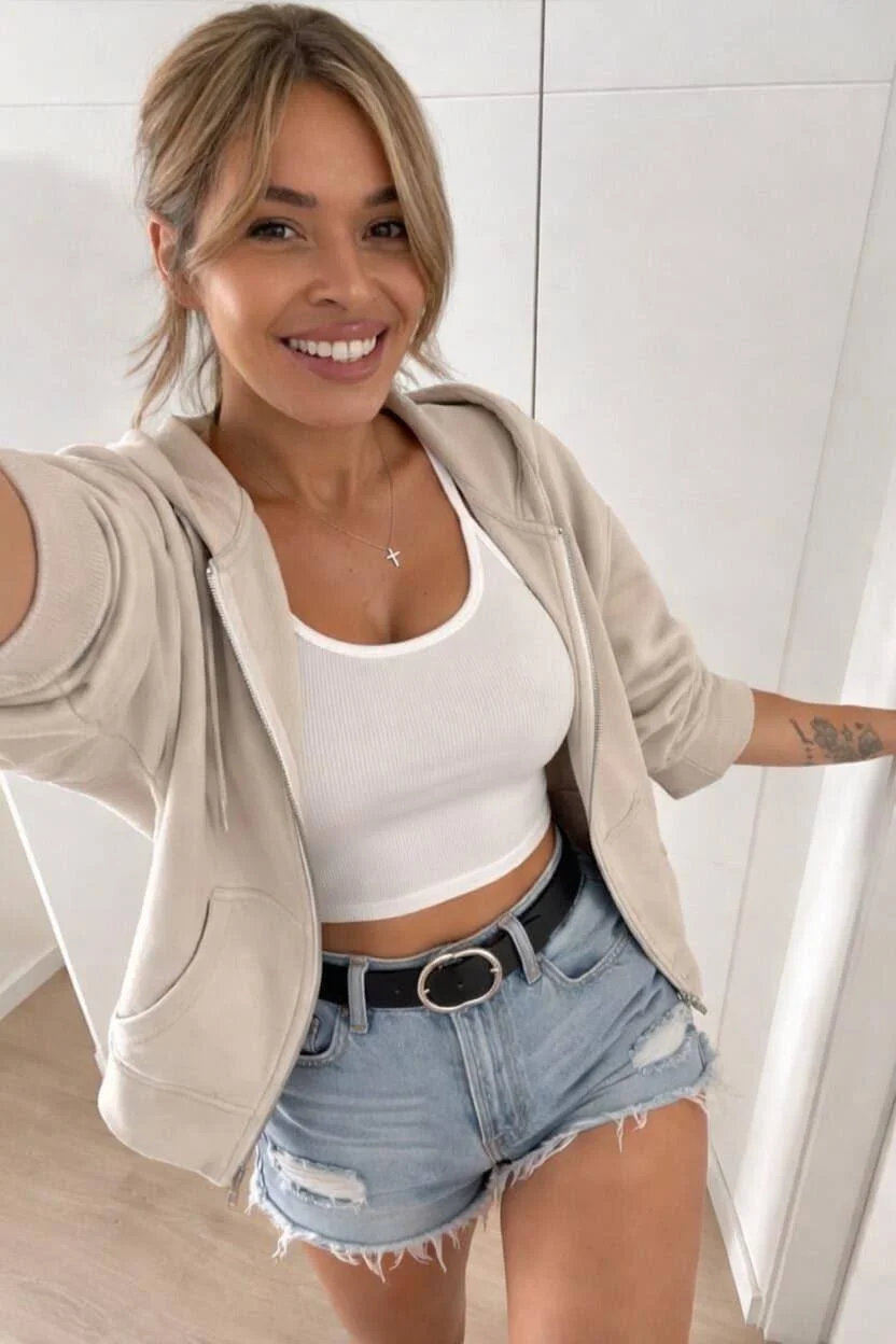 Smiling woman in white crop top and denim shorts.