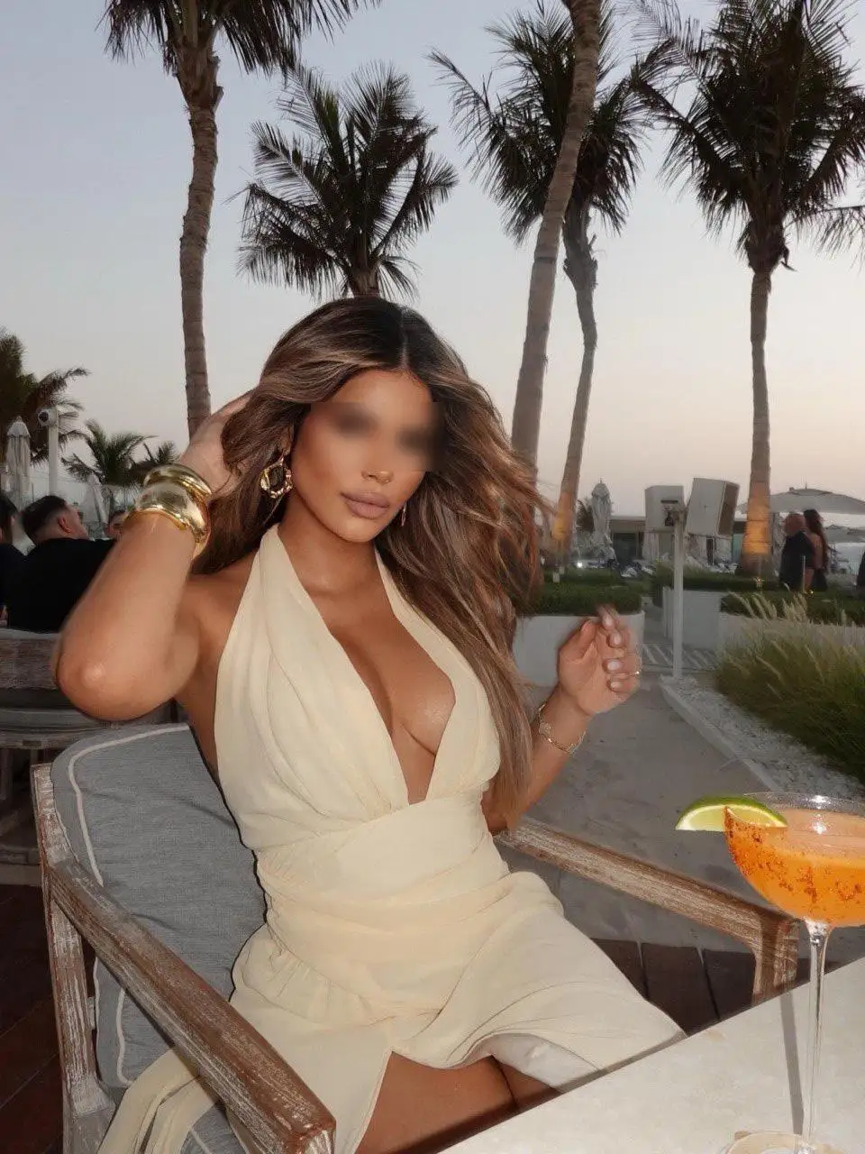 Woman in cream dress with cocktail, palm trees background.