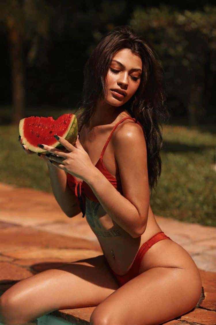 Woman in bikini eating watermelon by poolside.