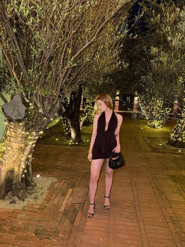Woman in dark dress standing on fairy-lit tree-lined path.