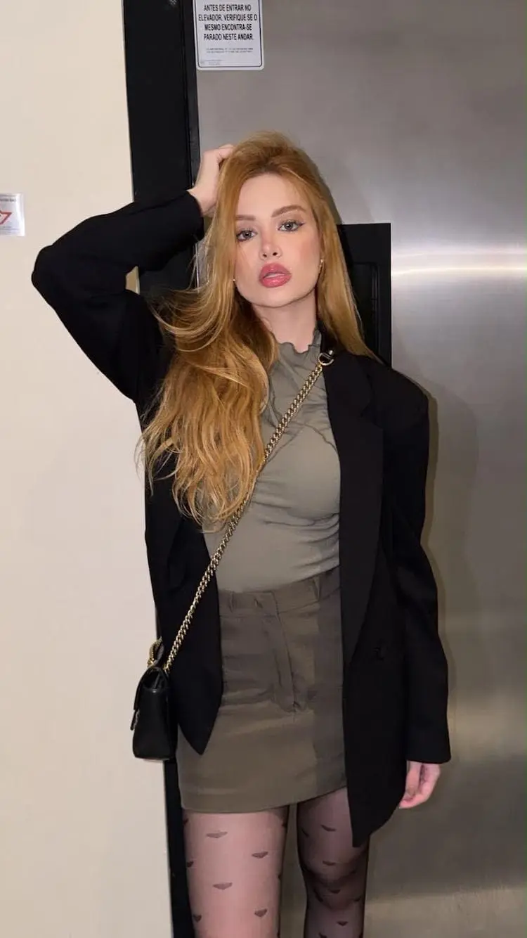 Woman with strawberry-blonde hair posing in an oversized black blazer.
