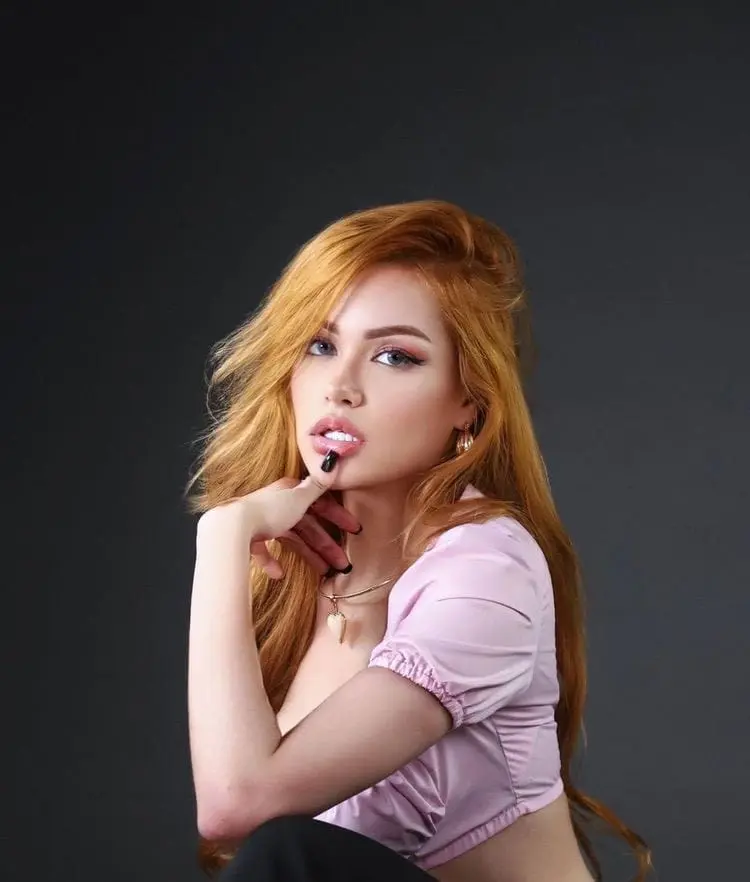 A woman with long red hair posing in a purple top.