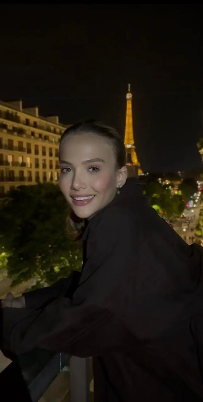 Smiling woman with the illuminated Eiffel Tower at night.