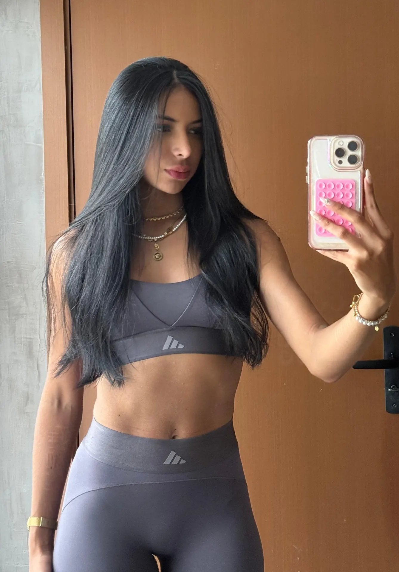 Woman in grey Adidas gym set taking a mirror selfie.