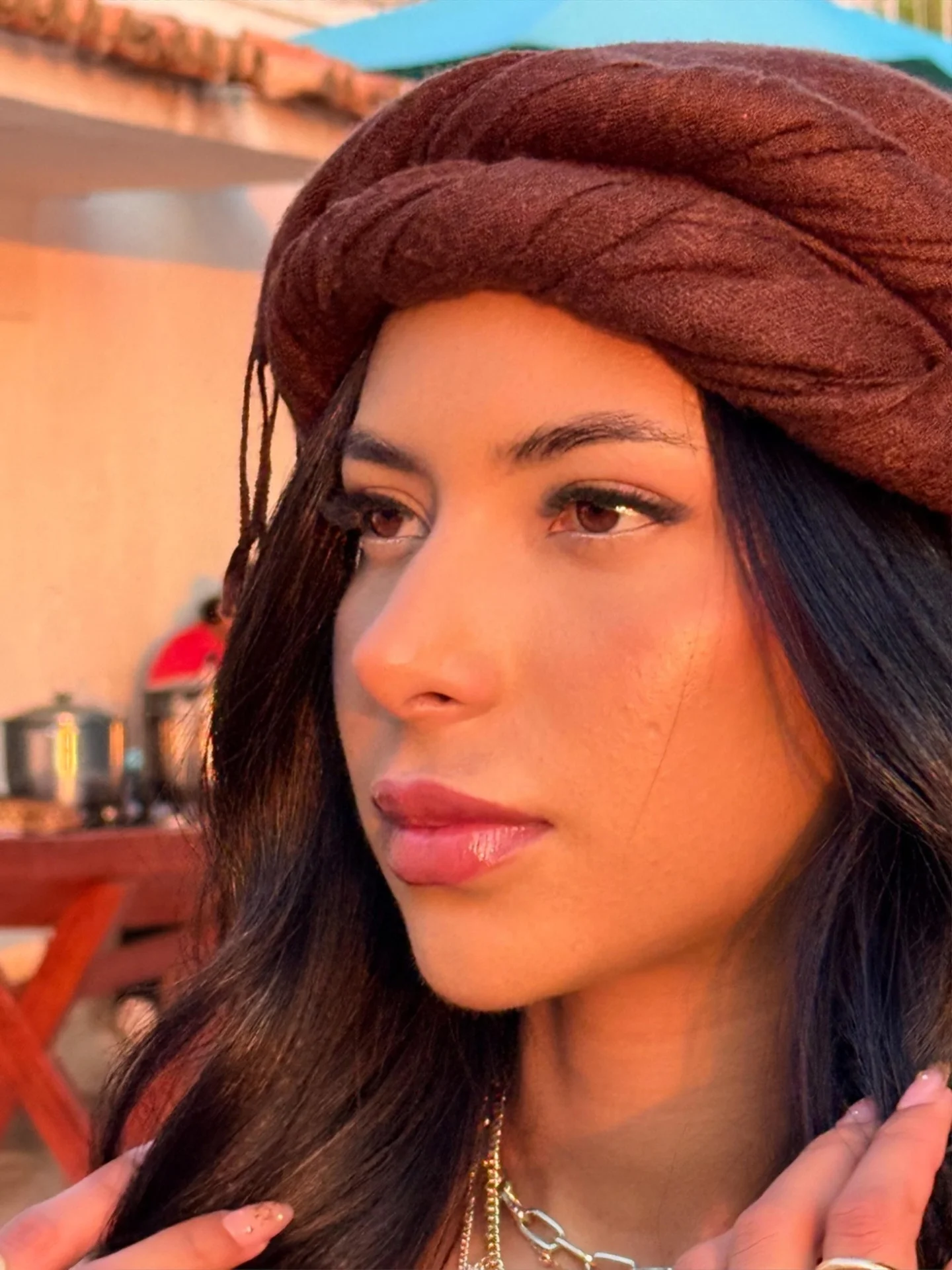 Woman with dark hair wearing a brown turban at sunset.
