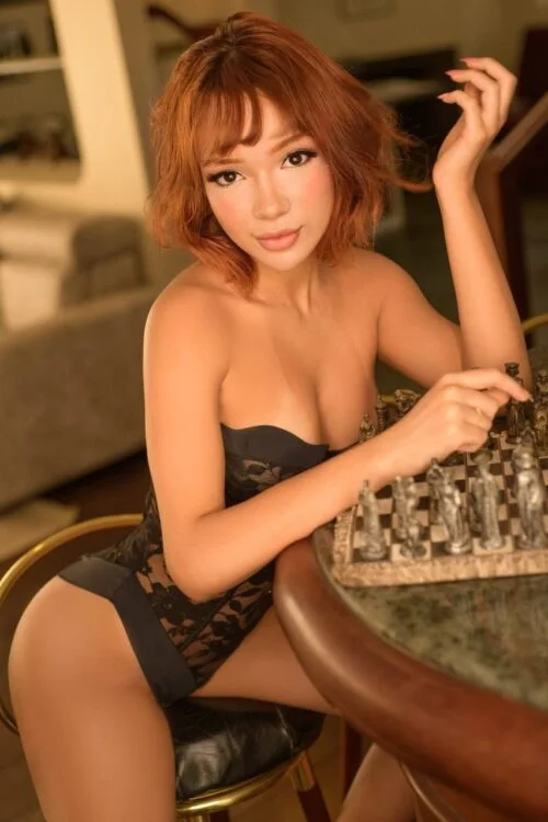 Woman with red hair in black lingerie at a chessboard