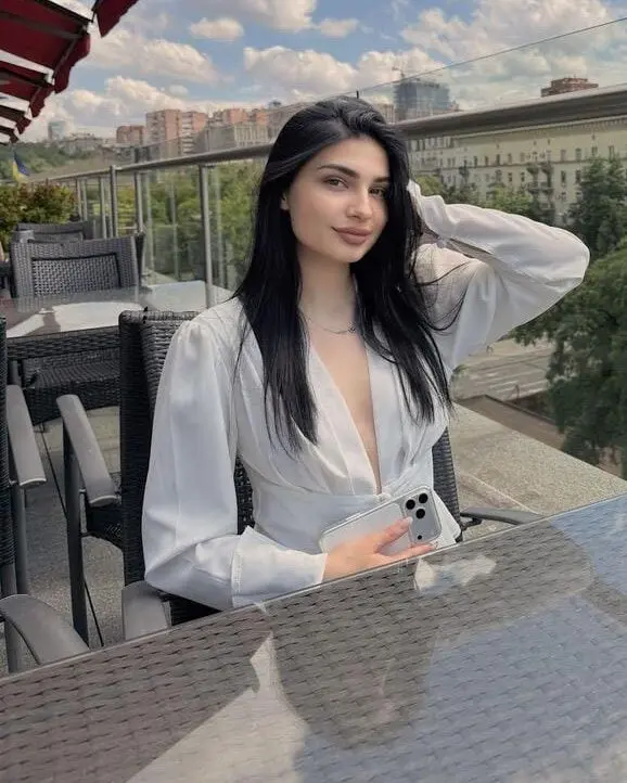 A woman in a white blouse sitting at a rooftop cafe.