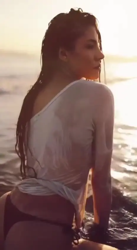 Woman in wet shirt on the beach at sunset.