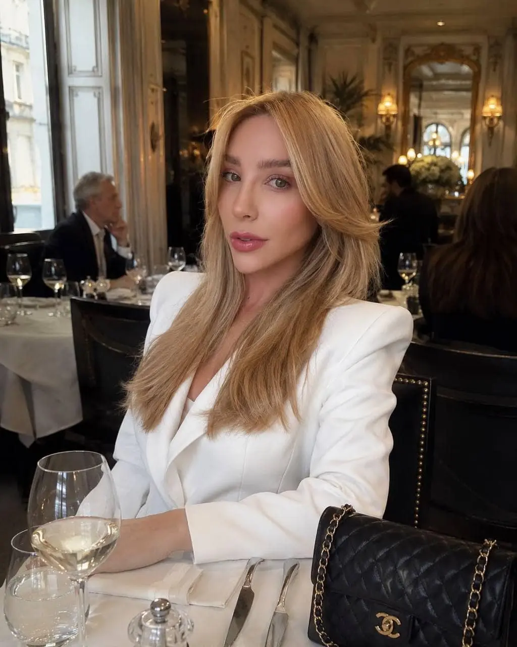 Blonde woman in white blazer at an elegant restaurant.