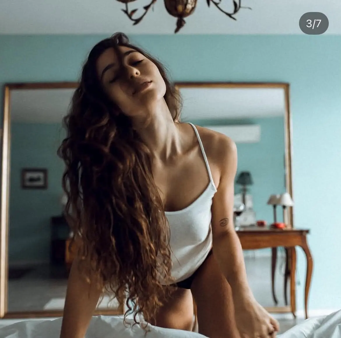 A young woman with long curly hair posing on a bed.