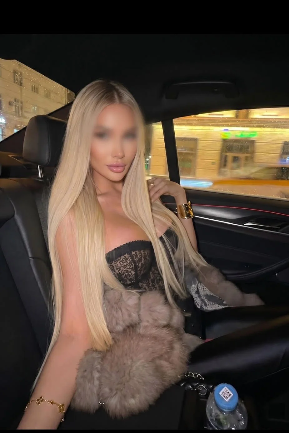 Blonde woman in black lace top in a car's backseat.