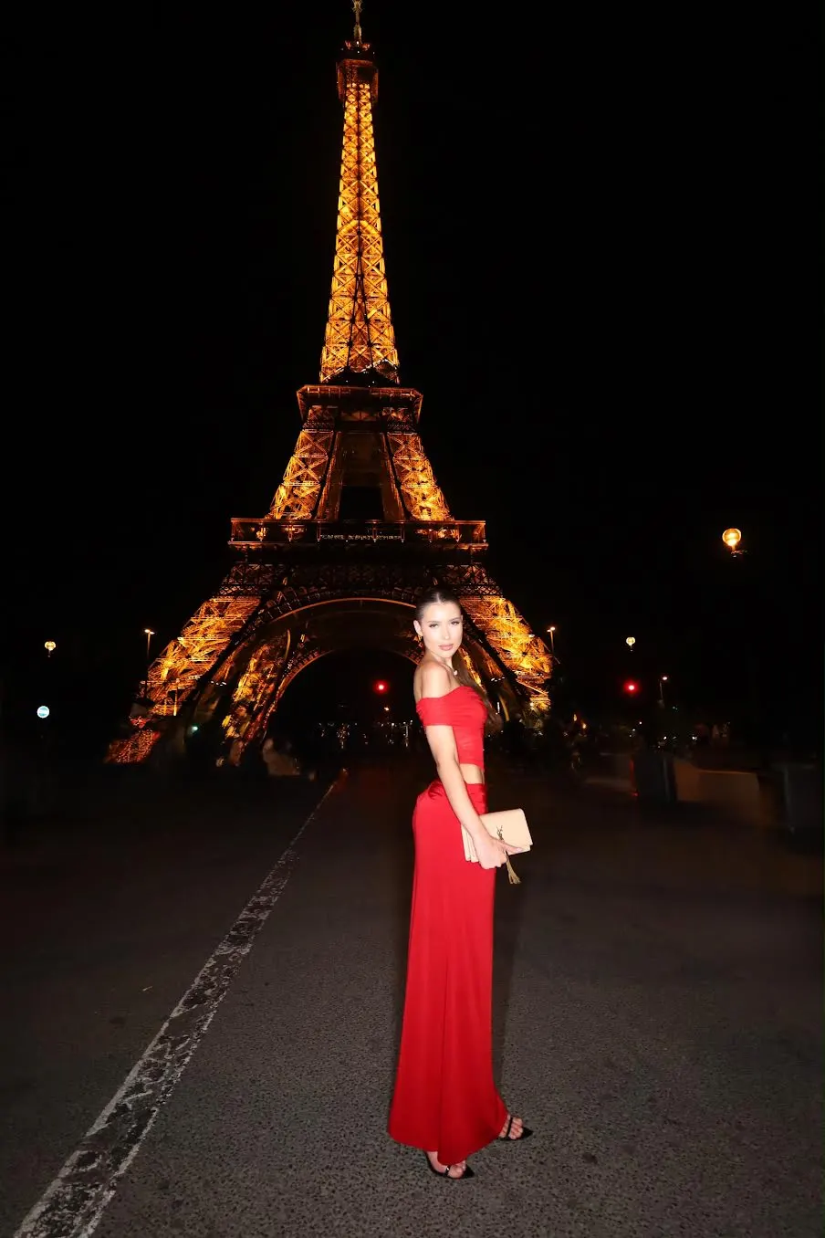 Woman in red dress posing before the illuminated Eiffel Tower
