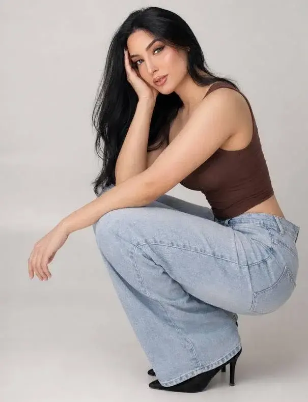Woman in brown top and light blue jeans posing.