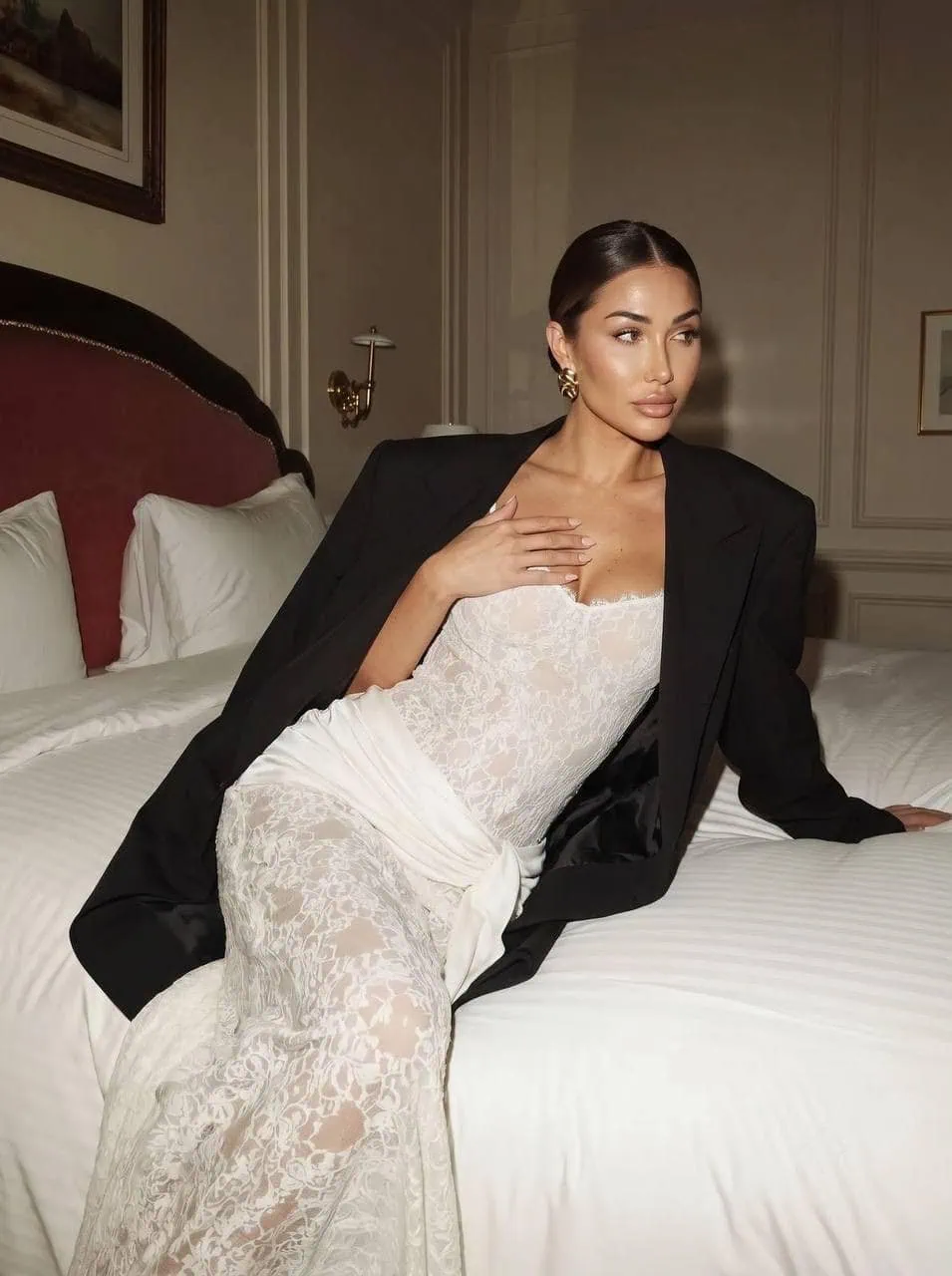 Woman in lace dress and oversized black blazer on bed.