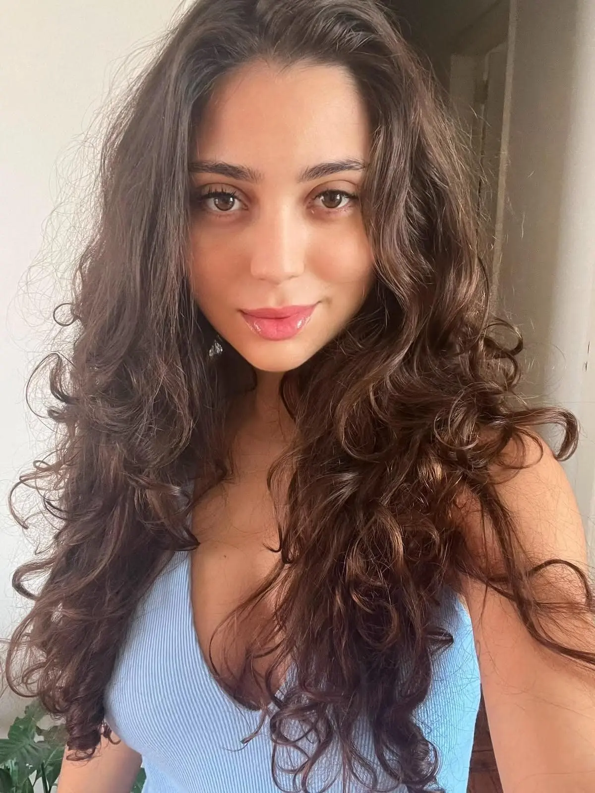 Young woman with long curly brown hair in a blue top.