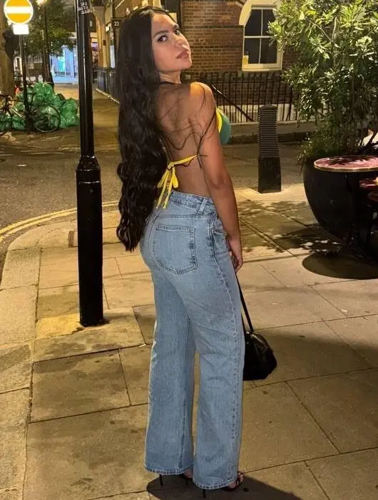 A woman with long dark hair posing on a pavement.