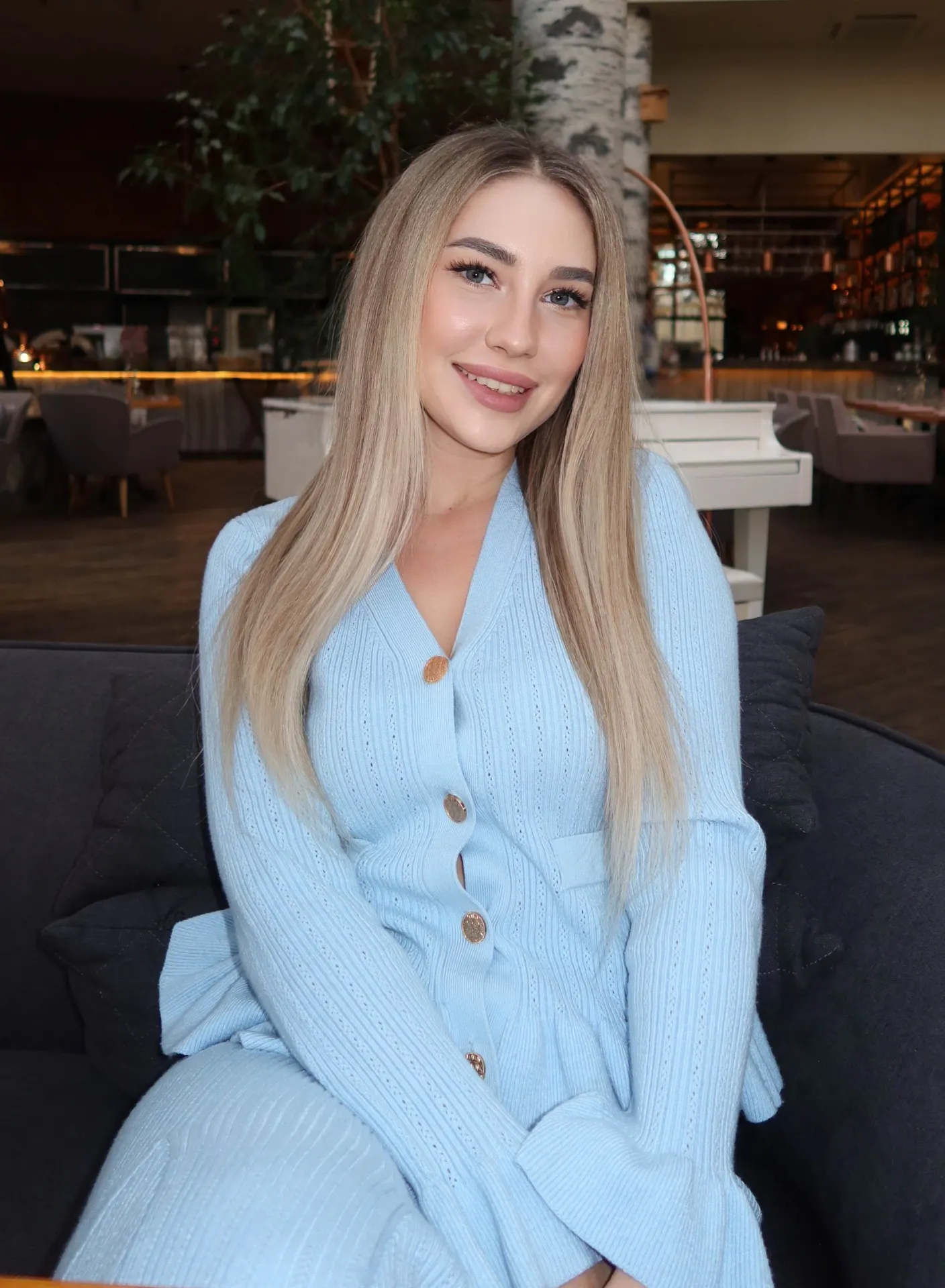 Blonde woman in a light blue knitted cardigan sitting down.