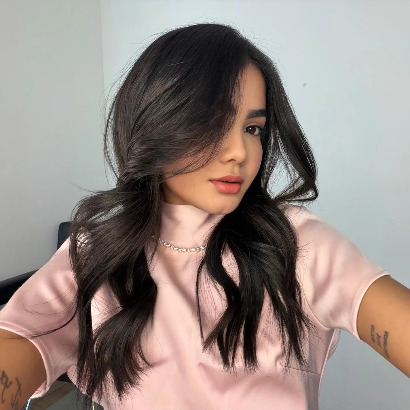 Woman with long dark wavy hair wearing a pink top