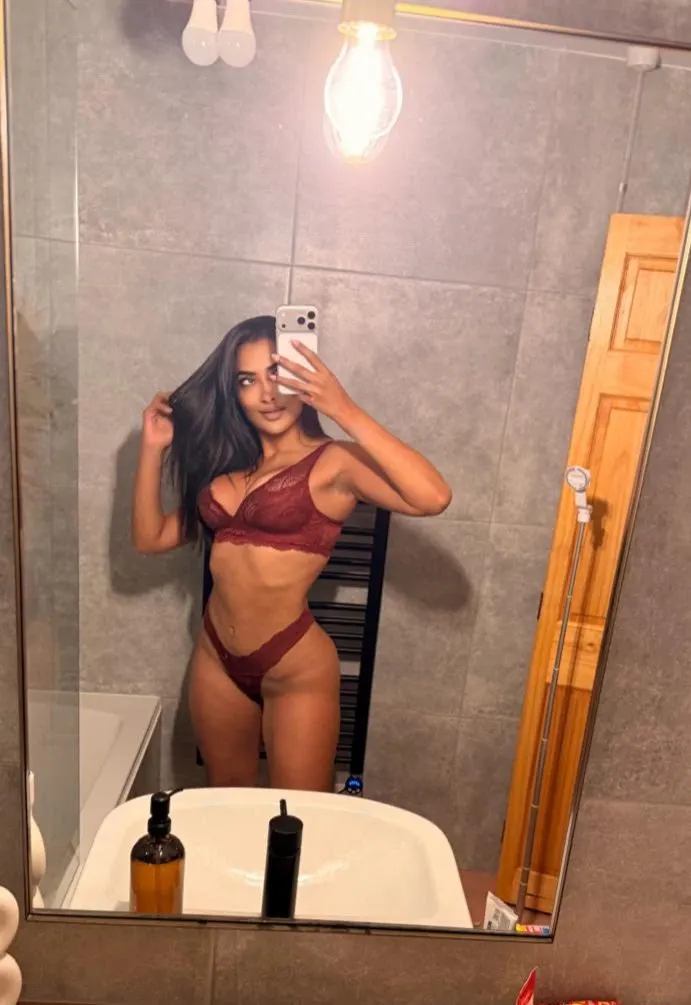 A woman posing for a mirror selfie in burgundy lingerie.