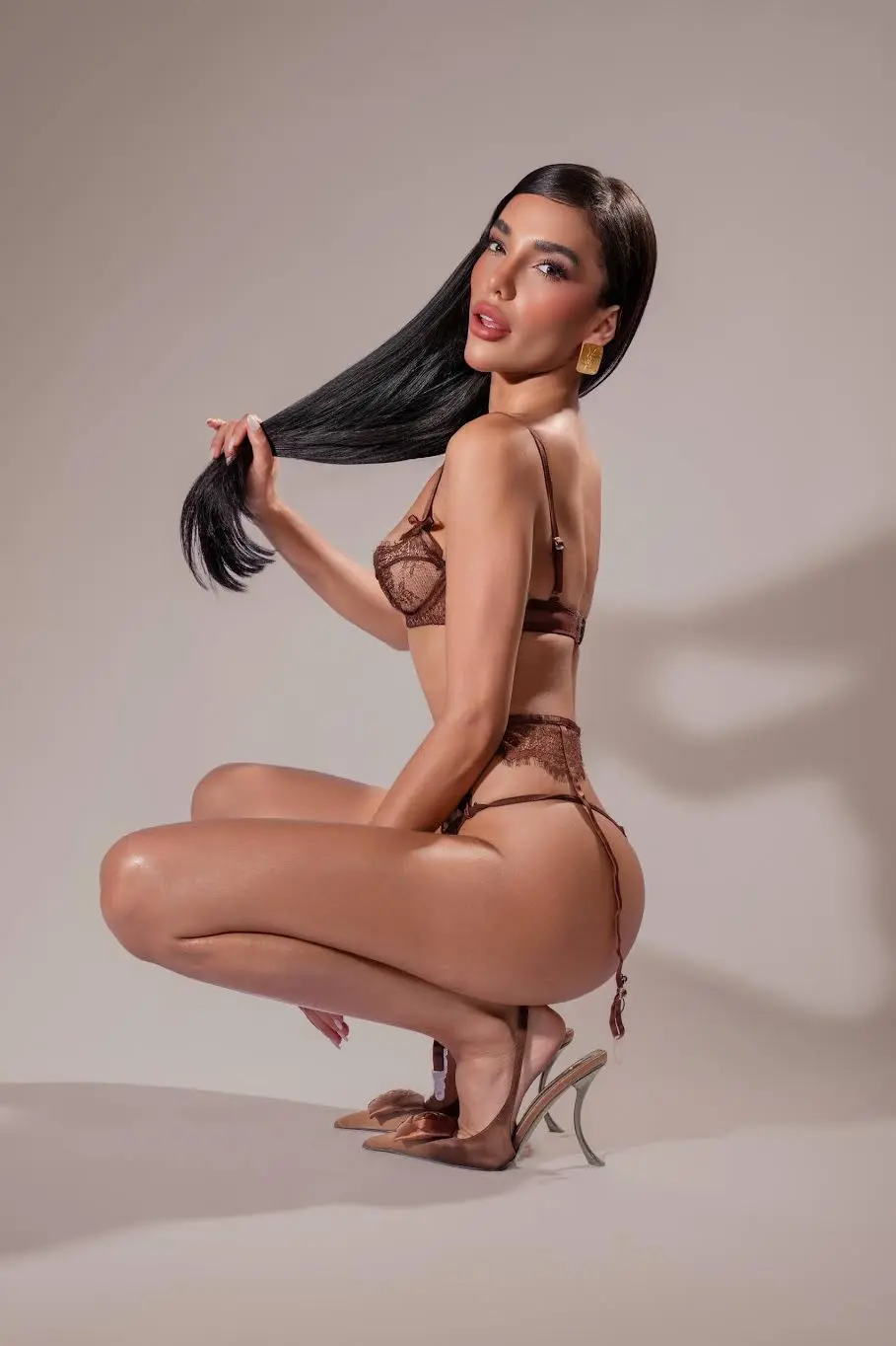 Woman in brown lace lingerie crouching against neutral background.