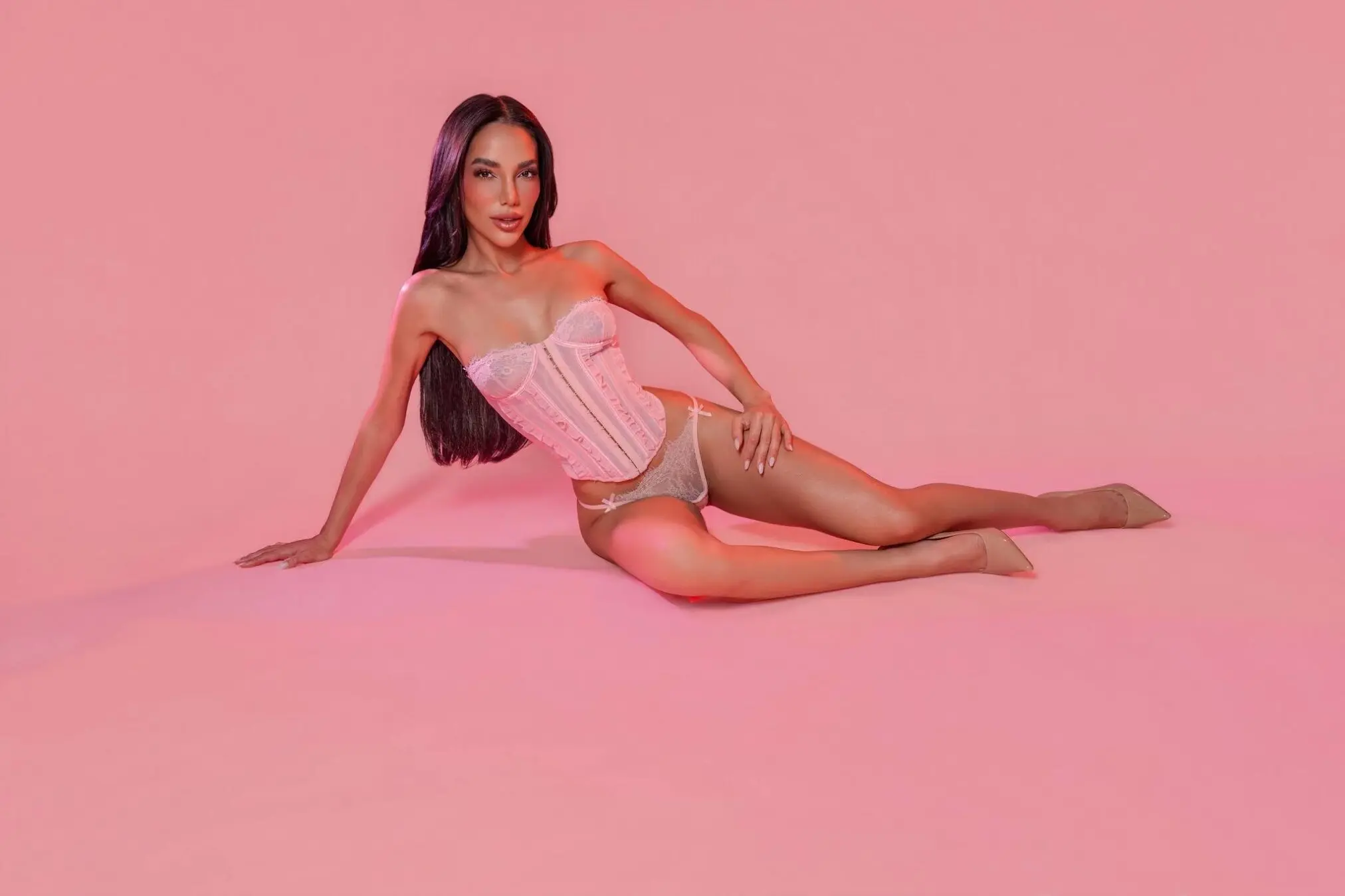 Woman in pink lingerie reclining against a pink background.